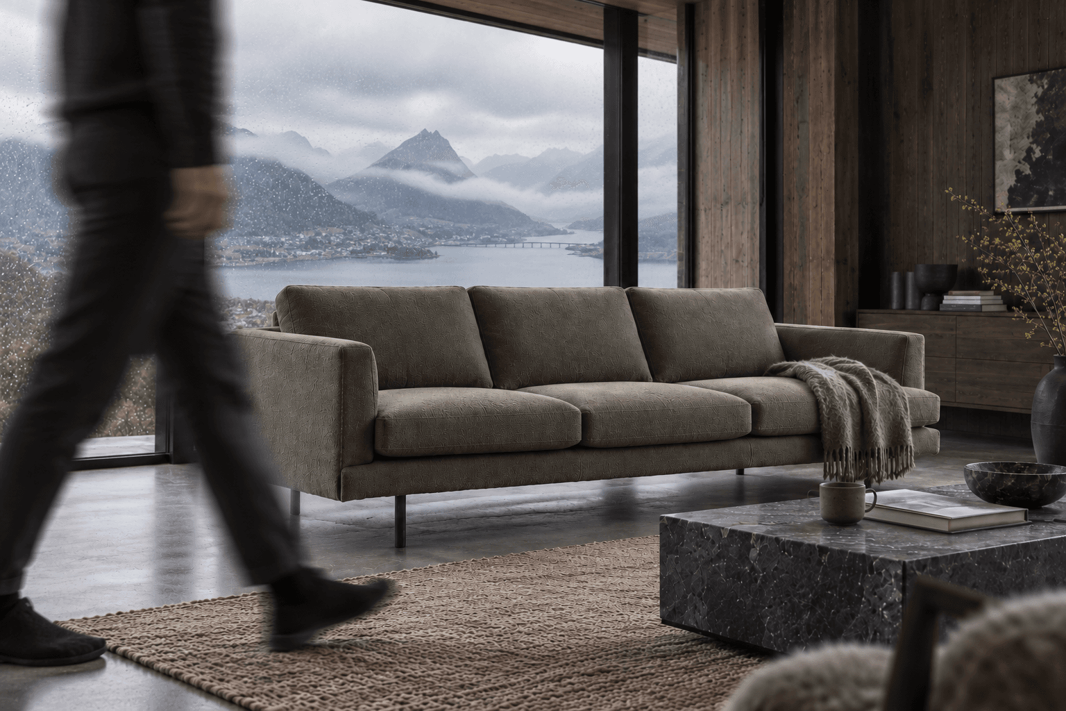 FRÍ sofa in a dark timber interior, with a person moving through the foreground.