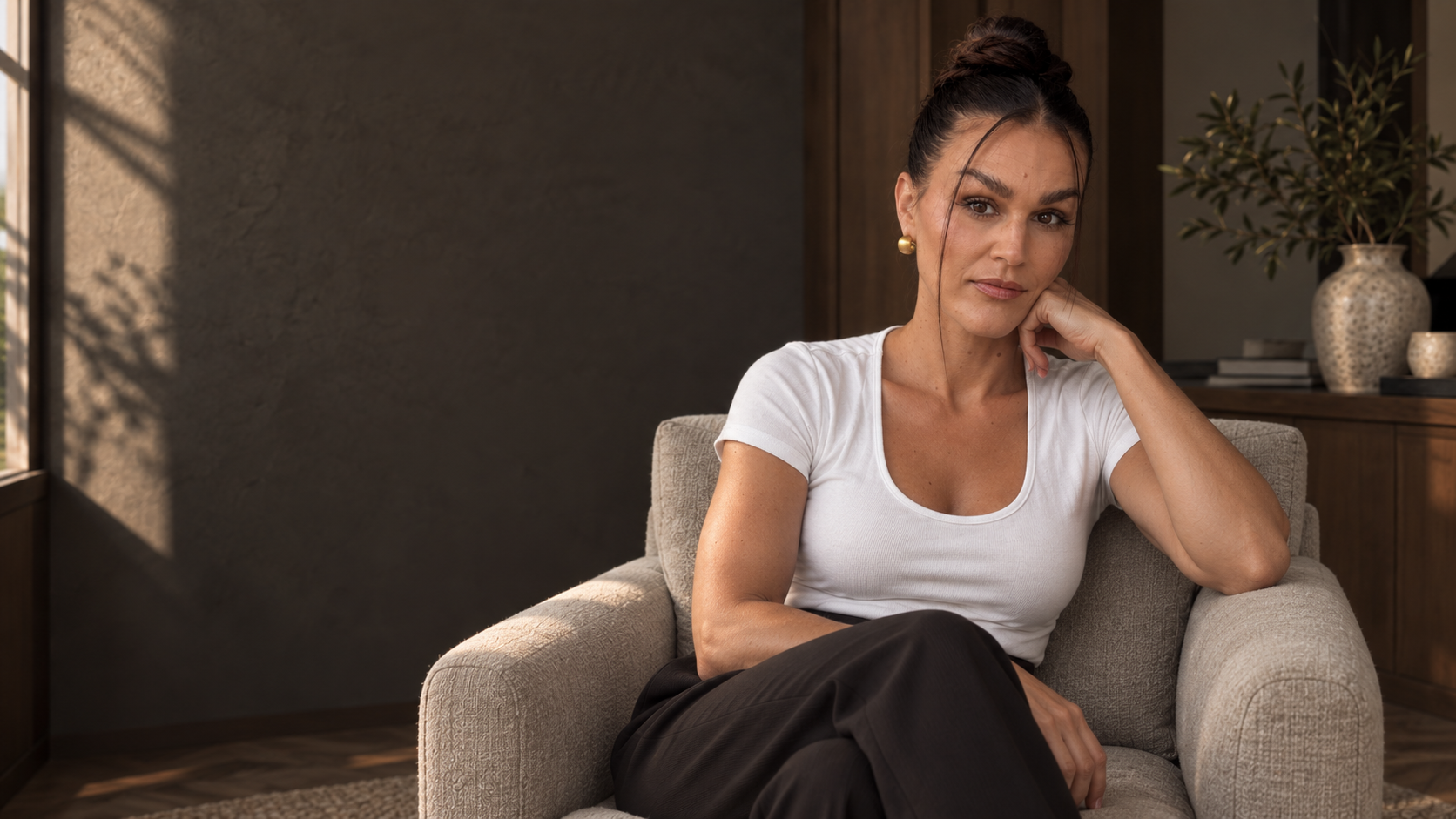 Sandra in a white cotton top, seated by a window in a dark oak and charcoal interior.